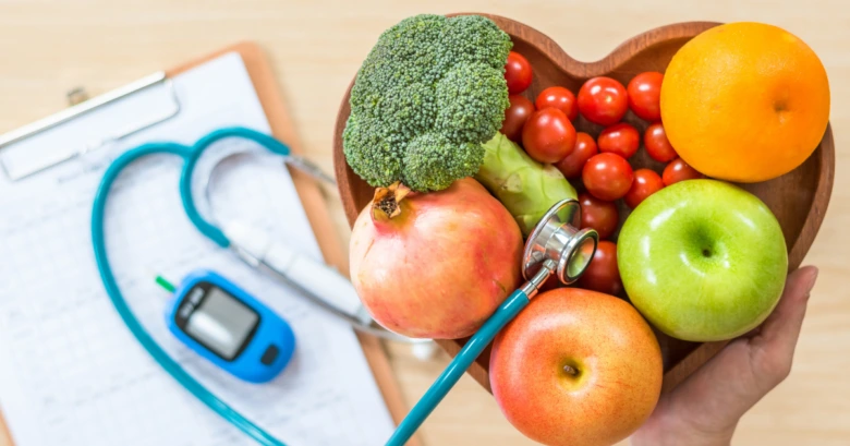 Ruce drží misku s ovocem vedle lékařských nástrojů pro kontrolu cholesterolu.