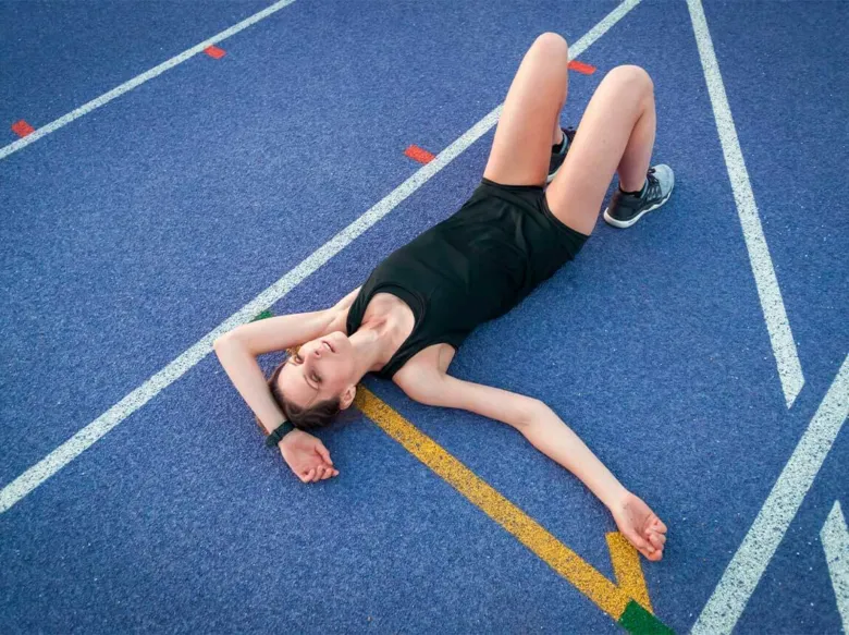 Žena leží na atletickém dráze po náročném tréninku.