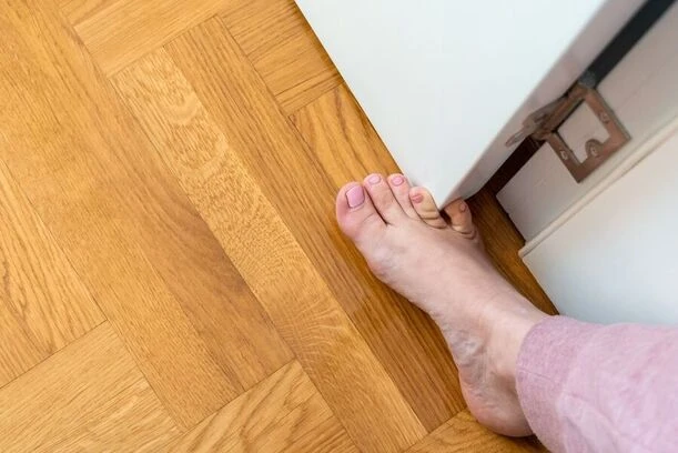 Holá noha na dřevěné podlaze u bílého nábytku.
