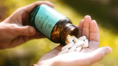 Ruce drží lahvičku s vitamínem B12, ze které se kapsle valí do dlaně.