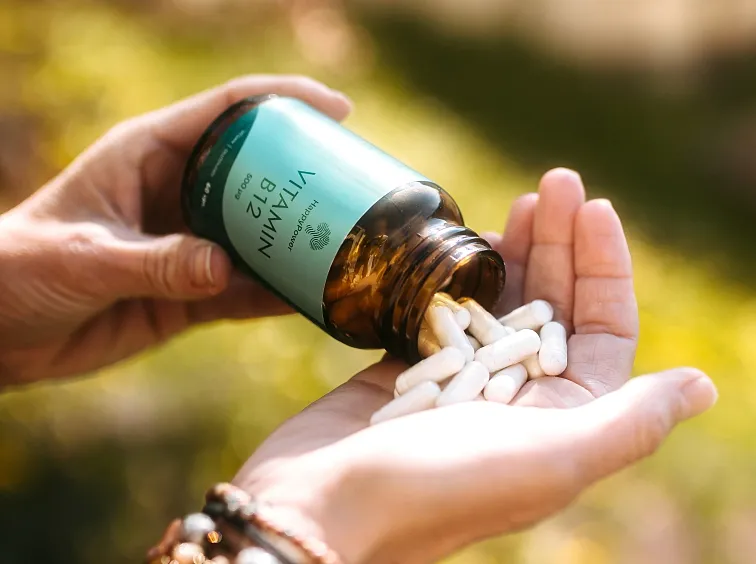 Ruce drží lahvičku s vitamínem B12, ze které se kapsle valí do dlaně.