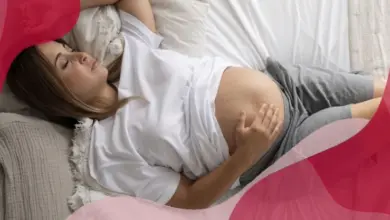 Těhotná žena leží na posteli a drží si břicho.