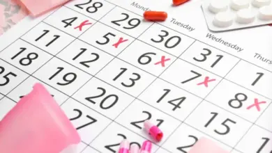 Kalendář s červenými křížky, antikoncepční pilulky a menstruační šálka.