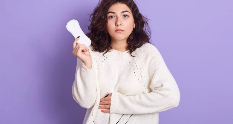 Žena drží menstruační vložku a stiská si břicho.