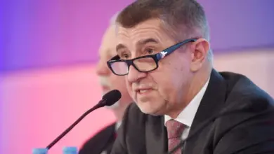 Muž v obleku mluví do mikrofonu na konferenci.
