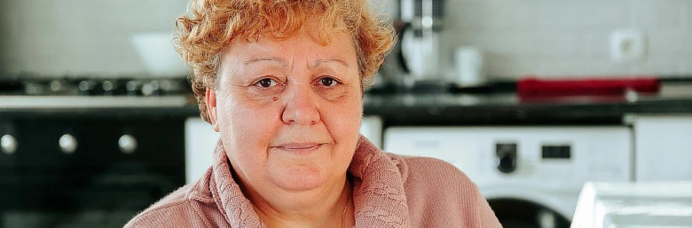 Žena sedící v kuchyni, ilustrační foto pro článek o příznacích.