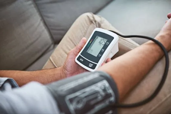 Muž měří krevní tlak doma pomocí digitálního přístroje.