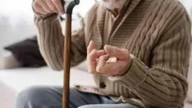Starší muž s holí ukazuje třes ruky jako příznak Parkinsonovy nemoci.