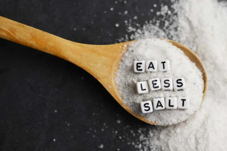 Dřevěná lžíce s solí a písmeny Eat Less Salt.