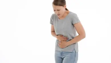 Žena drží břicho v bolesti na bílém pozadí.