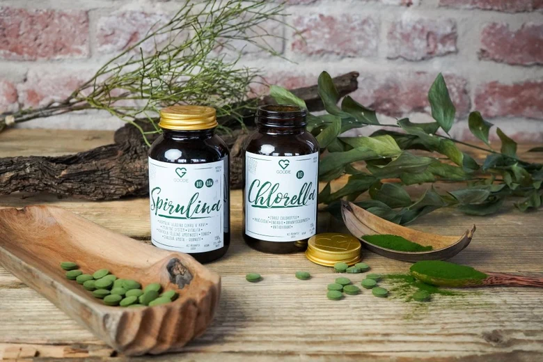Doplňky spiruliny a chlorelly na dřevěném stole s bylinkami.