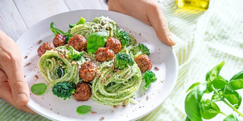 Pasta s masíčky brokolicí bazalkou na bílém talíři.