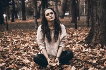 Žena sedí na podlaze z listů v lese.