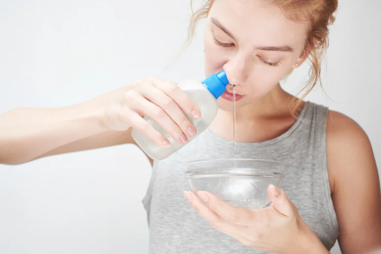 Žena vyplachuje hrdlo tekutinou z láhve do mísy.