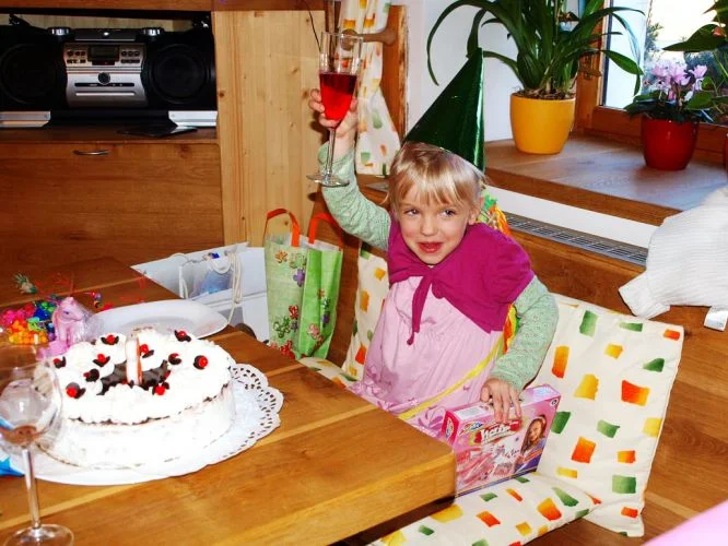 Dívka slaví narozeniny s dortem a dárkem v interiéru.