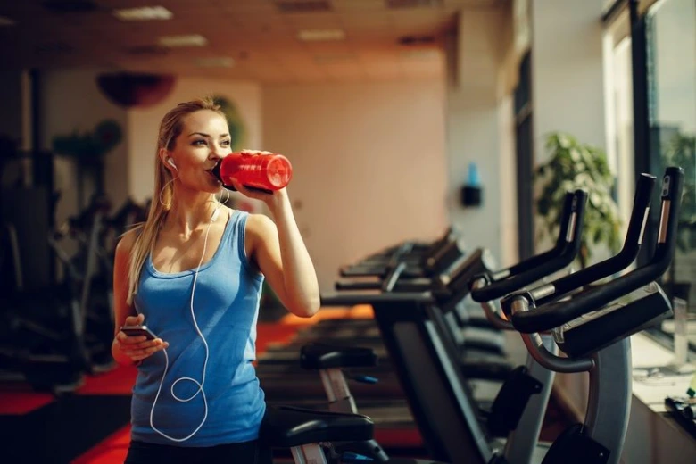Žena pije vodu během cvičení ve fitness centru.