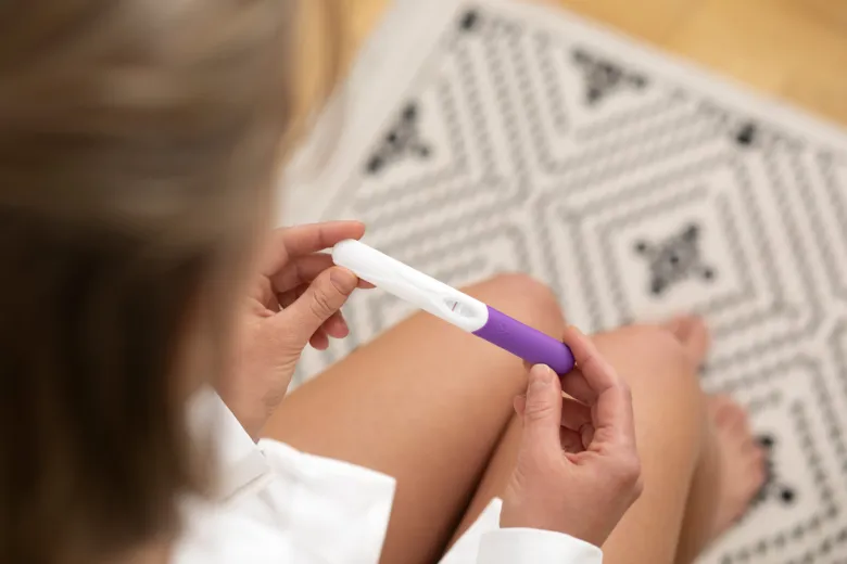 Žena drží těhotenský test s pozitivním výsledkem.