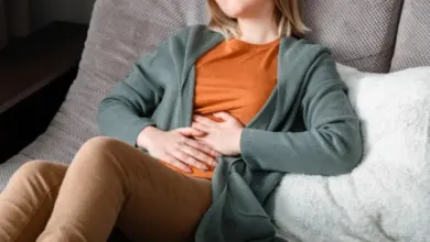 Žena sedí na gauči a drží si břicho rukama.
