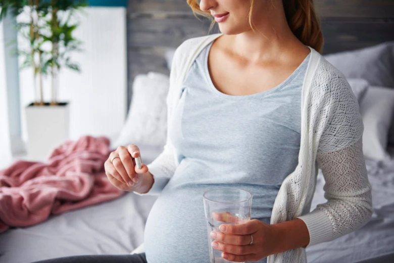 Těhotná žena bere vitamin s vodou na posteli