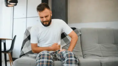 Muž sedí na gauči a drží si břicho kvůli bolesti.