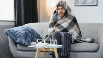 Muž zabalený v dečce sedí na gauči s příznaky chladu.