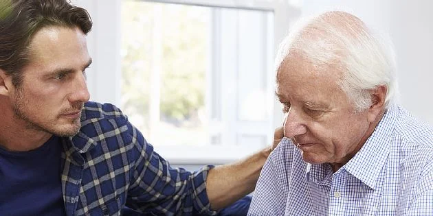 Mladý muž utěšuje staršího muže s Alzheimerovou chorobou.
