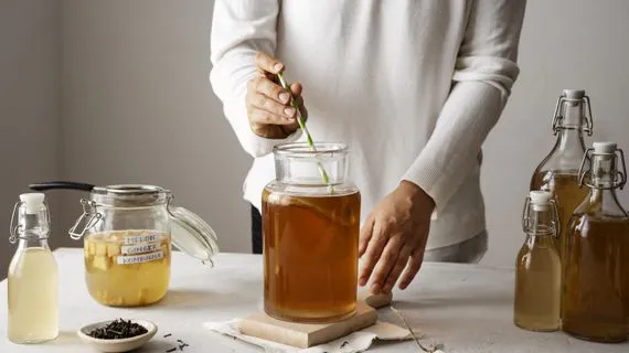 Osoba míchá fermentovaný nápoj v skleněné dóze s dalšími láhvemi.