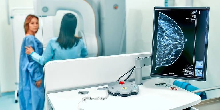 Žena v modrém plášti u mamografu s výsledkem na displeji