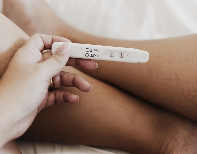 Ruka drží těhotenský test s pozitivním výsledkem.