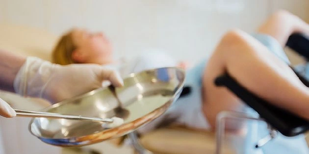 Zdravotnický pracovník s kovovým podnosem při gynekologickém vyšetření