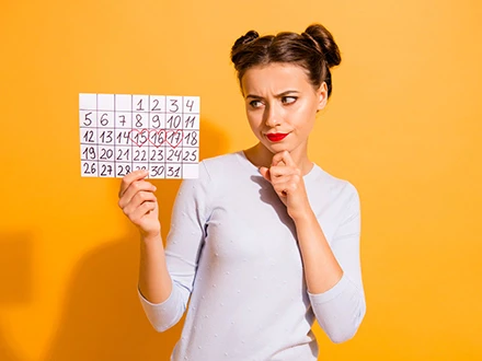 Žena drží kalendář s daty, zatímco přemýšlí o menstruačním cyklu.
