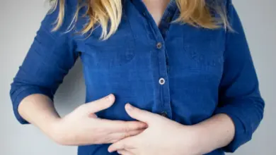Žena drží břicho v modré košili kvůli bolesti.