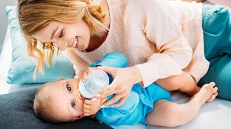 Matka krmití dítě fľaškou s modrou fólií.
