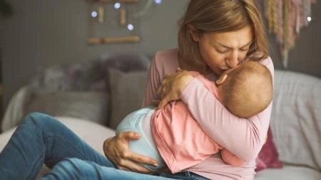 Matka drží své novorozence v náručí na posteli.