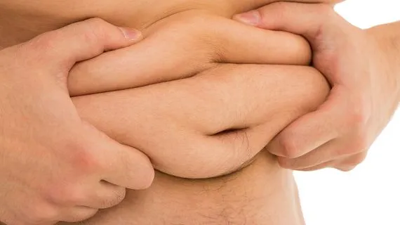 Ruce stiskající vrstvu podkožního tuku na břiše pro měření.