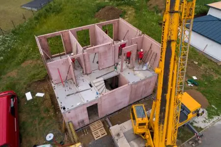 Stavba domu z keramického betonu s žlutým kranem.