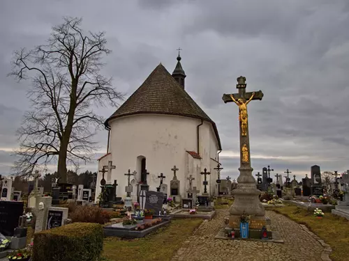 Starý kostelík na hřbitově s kříži pod šedou oblohou.